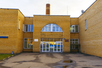 Yellow brick institutional building entrance with arched window, glass doors, and symmetrical facade © ossyffer