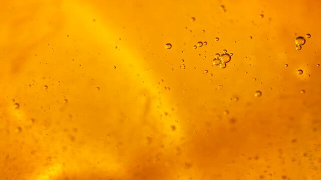 Golden oil bubbles float through an amber liquid in a glowing macro. Concept food branding, cosmetic packaging, banners, websites and abstract advertising.