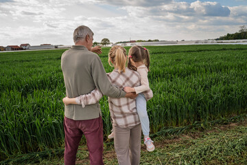 Obraz premium Back view, three generations in one family on agricultural field, grandfather his daughter and and his grand daughter 