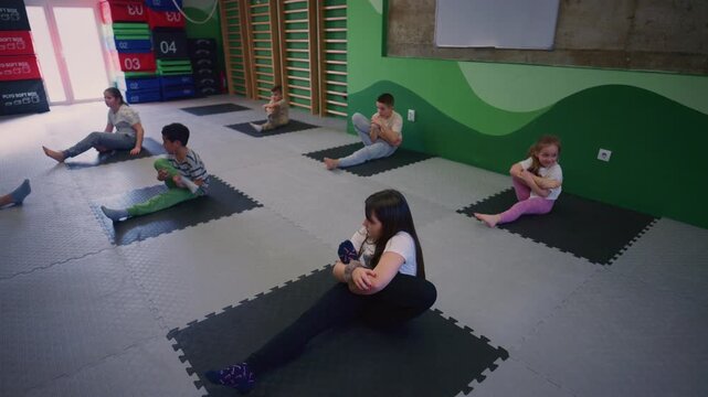 A group of young children actively participates in a stretching and flexibility session. Kids are engaged in various exercises on mats, promoting their physical development.