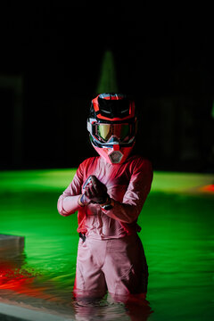 Person in red riding gear standing in a neon green swimming pool during the dark night hours