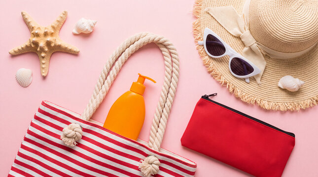 Top view of summer beach vacation accessories including a straw hat, striped tote bag, sunscreen, sunglasses, and seashells on a pink background.