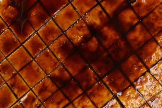 A full frame macro shot focusing on a cross scored round slice of celeriac root glazed with thick dark brown marinade sauce.