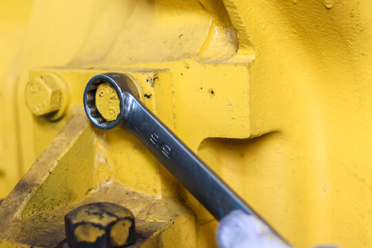Ring spanner tightening a bolt on heavy yellow machinery.