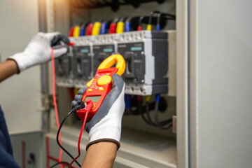 Obraz na płótnie Canvas professional industrial electrician hands holding digital clamp meter and configuring test probes inside commercial circuit breaker panelboard.