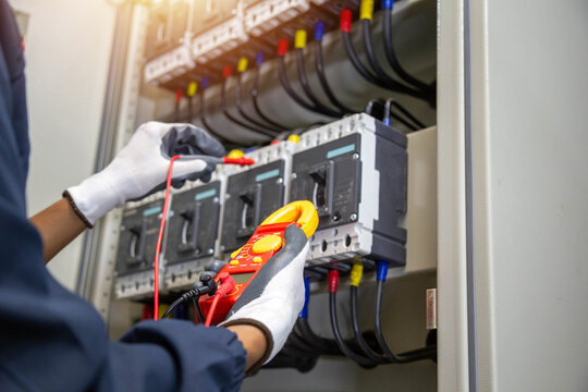 Electrician using digital clamp meter to check circuit breaker panel.