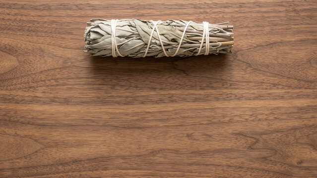 Bundle of dried sage smudge stick tied with string on a wooden background with copy space