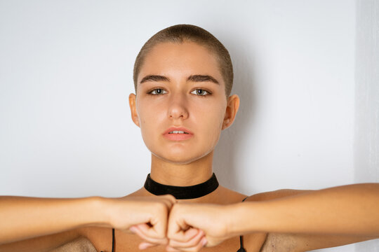 Close portrait of a young caucasian woman with a shaved head and a black choker at a white wall, for motivation, willpower and inclusive casting content