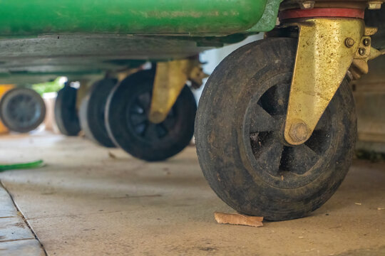 Low angle close up view of heavy duty black rubber swivel caster wheels mounted under commercial green waste dumpsters on a tiled floor.