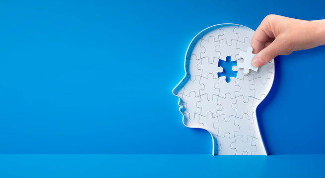 Conceptual artwork showing a 3D silhouette of a head with puzzle pieces, a hand holding one puzzlepiece, symbolizing mental activity, intelligence, or creativity - 3D illustration on blue background	