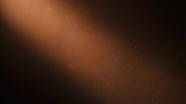 Warm copper dust drifts and swirls through diagonal backlight, particles catching soft glow against deep black with dreamy industrial atmosphere, cinematic depth, and gentle motion.