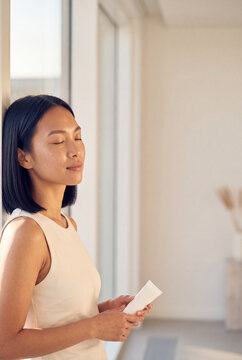 Relaxed woman with eyes closed holding skincare tube by window in calm natural light for beauty and wellness lifestyle banner and morning routine imagery