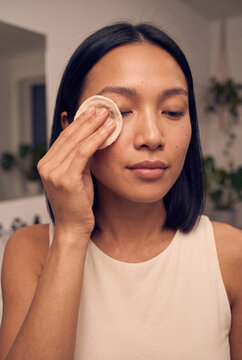 Young woman removing makeup with reusable cotton pad for skincare routine and gentle cleansing tutorial background