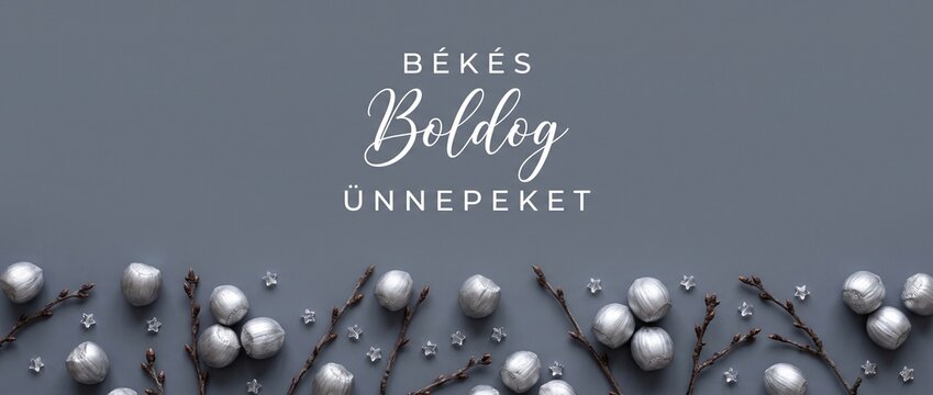 Hungarian holiday banner background with silver painted hazelnuts and twigs, featuring B&eacute;k&eacute;s Boldog &Uuml;nnepeket Hungarian greeting text for winter Christmas season header card layout. Happy Holidays.