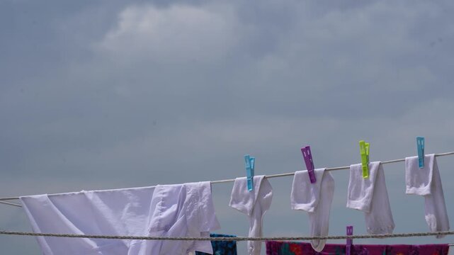 White laundry hanging on a clothesline with colorful pegs against a cloudy sky.