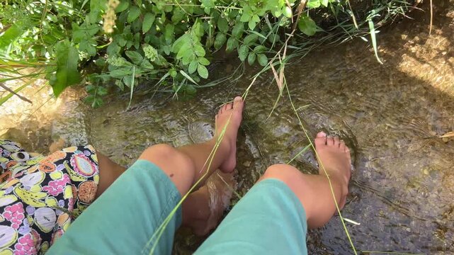 High angle view of a young boy and girl wading and splashing their feet in a clear shallow stream surrounded by lush green vegetation on a sunny summer day