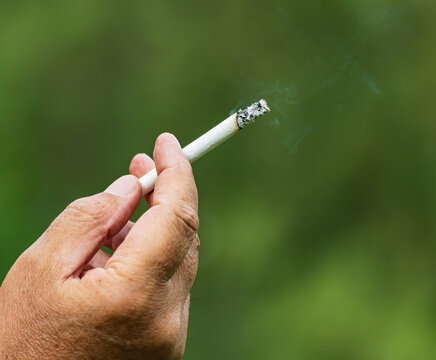 Hand holds cigarette with smoke rising