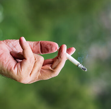 Hand holds cigarette with smoke curling gently upward