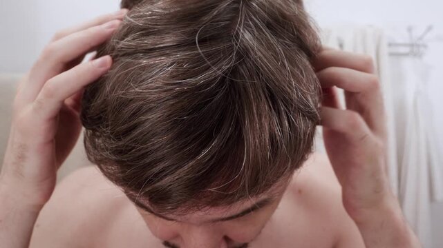 Man checking his hair thickness and scalp, noticing gray hairs and signs of thinning