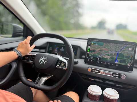 Driver holding the steering wheel inside a modern car, with gps navigation on the dashboard, coffee cups in the console and a blurred road ahead. MG S5 EV electric Poland, Pszczyna, 3.08.2026 

