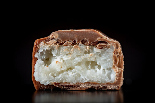 Chocolate bar cross section with coconut filling on black background, macro, Chocolate bar cut in half showing detailed layers of milk chocolate and moist white coconut flakes filling, closeup