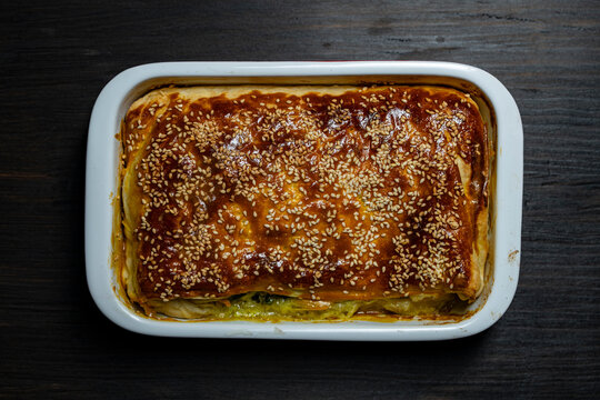 Freshly baked homemade pie with sesame seeds in baking dish, close up. Top view of golden crispy pastry pie topped with sesame in ceramic pan on wooden background healthy delicious dinner food concept
