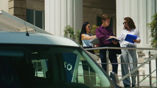 A small team of colleagues reviews documents and a tablet outdoors. They engage in a focused discussion, examining paperwork together.