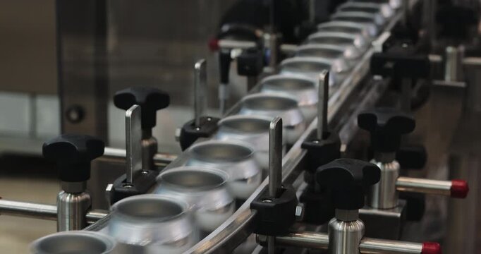 Empty aluminum cans pass through straight conveyor section in industrial plant. Precision guides control alignment carrying containers toward filling station
