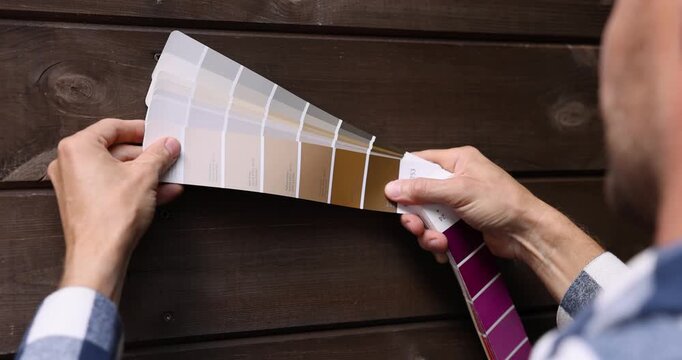 man choosing paint color from samples palette for wooden plank house exterior cladding