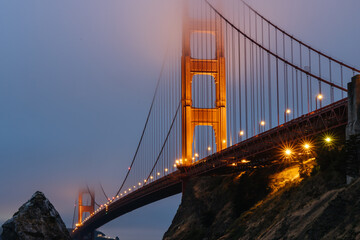 Fototapeta premium Illuminated Golden Gate Bridge tower in San Francisco Bay fog seen from Fort Baker