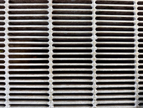 Close-up of a metal drainage grate with repeating horizontal lines, creating an industrial geometric texture and abstract background.

