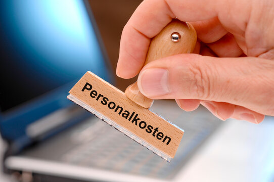 Eine Hand h&auml;lt einen Holzstempel mit dem Aufdruck Personalkosten