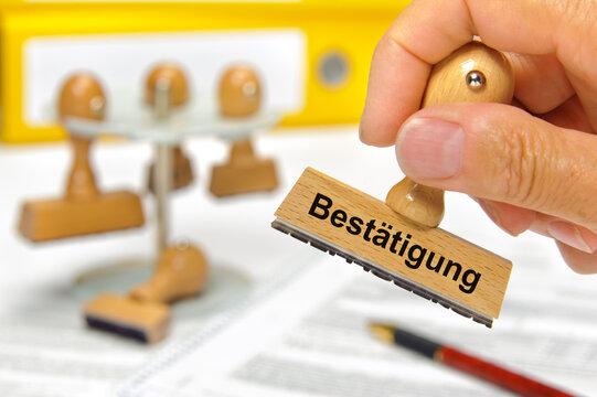 Eine Hand h&auml;lt einen Holzstempel mit der Aufschrift: Best&auml;tigung