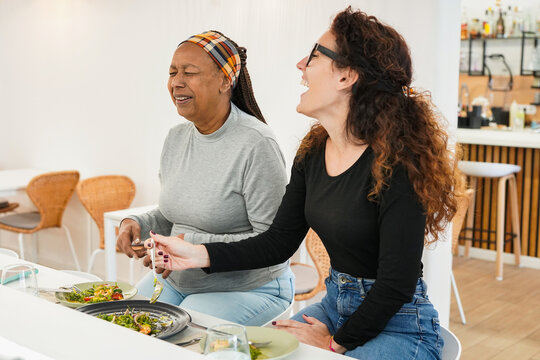 Happy multiracial women with different age sharing healthy food during lunch time at modern restaurant - Female friendship, multi generational people and lifestyle concept