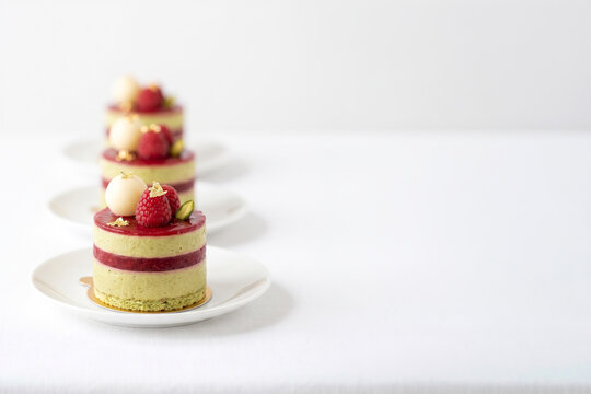 Pistachio bavarois mousse with red fruit insert, topped with white spherification, raspberries, and gold leaf details. A sophisticated modern mini dessert served on a delicate white plate.