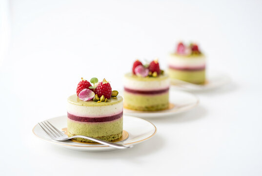 Refined layered pistachio and raspberry bavarois decorated with fresh raspberries, gold leaf, and edible pink petals. An elegant single-portion dessert for modern high-end pastry presentation.