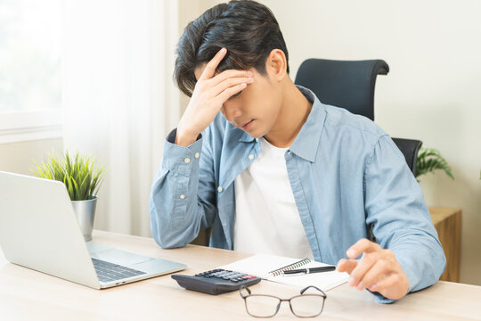 Exhausted, asian young businessman work at office desk, male took off eye glasses, headache from migraine, suffer on work hard, using laptop computer at office home, overtime job. Health care concept.