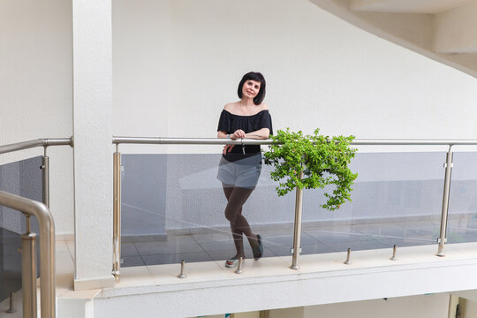woman wearing a stylish black blouse and white shorts posing indoors against clean white walls inside a bright modern building.