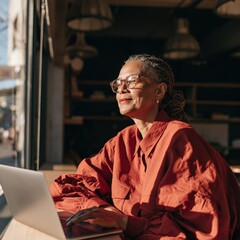 Obraz premium Woman with laptop in sunny cafe workspace with warm light for remote work background and professional banner