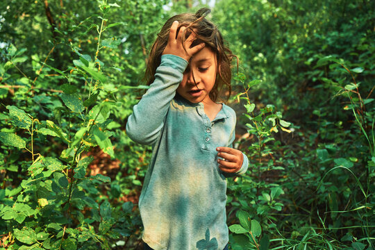 Boy pushing hair from his face while standing in thick bushes