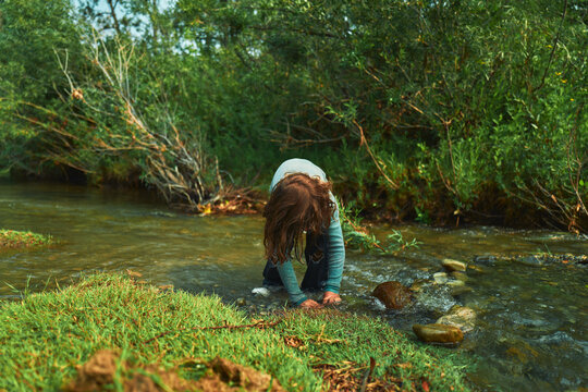 Boy crouching at a river edge with hands in the water