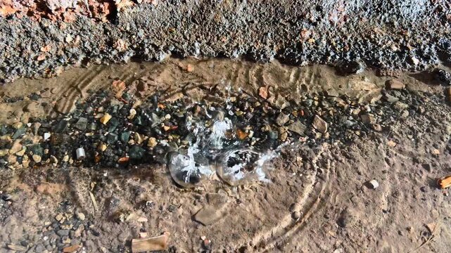 Raindrops create circular ripples in muddy puddle beside rough tunnel wall