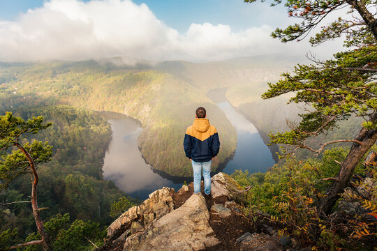 Rear view of tourist standing at scenic Maj viewpoint and looking at famous horseshoe bend of Vltava river. Czech Republic travel destination, canyon landscape and outdoor exploration concept.