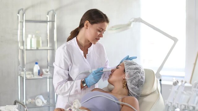 Young female aesthetician making facial beauty procedure with leather knife attachment to brunette girl. High quality 4k footage
