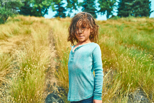 Boy with windswept hair standing on a hillside path facing the camera