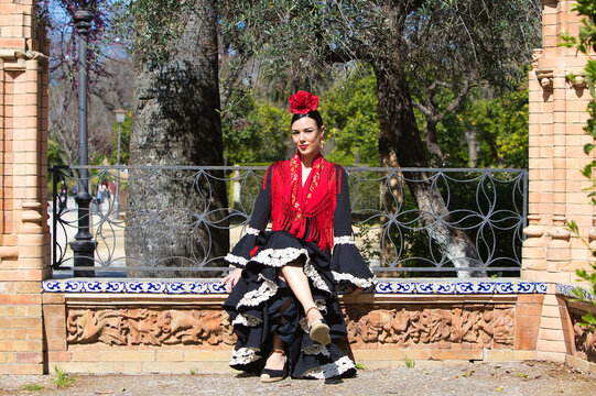 A beautiful flamenco dancer sitting on a tiled bench in a square in Seville, Spain. She is wearing a black ruffled dress and a shawl. Flamenco, a UNESCO Intangible Cultural Heritage.