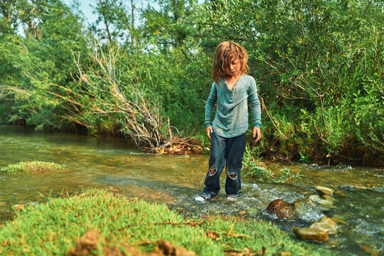 Boy standing in a shallow river looking down at the water