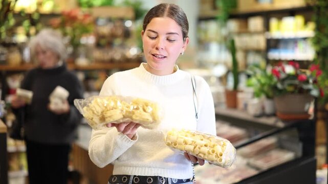  Young woman buyer chooses pasta in package in eco grocery supermarket