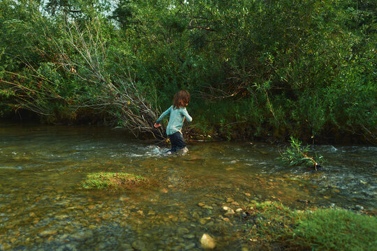 Boy wading alone in a river toward the far bank
