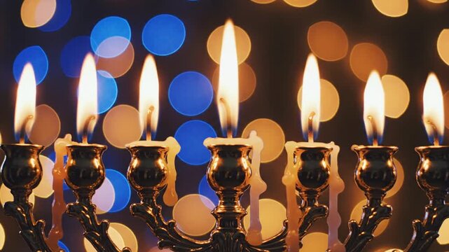 Burning Hanukkah menorah candles with blue and gold bokeh lights